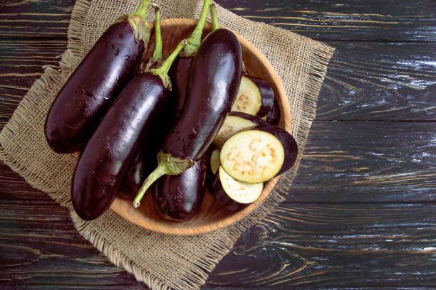 A bunch of fresh purple brinjals (eggplants) on a wooden surface, ready for cooking.