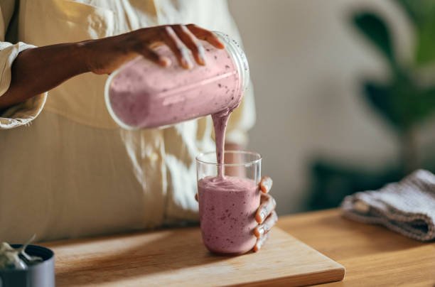A close-up image of a spoonful of powdered stabilizer being added to a creamy dessert mixture.