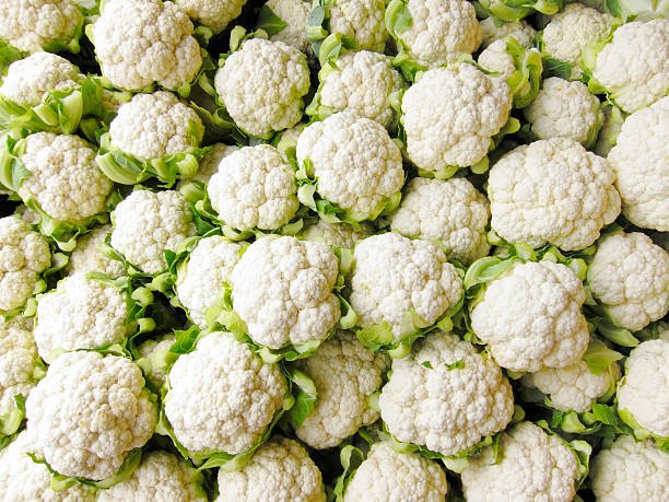 A close-up of fresh white cauliflower florets on a cutting board with a knife.
