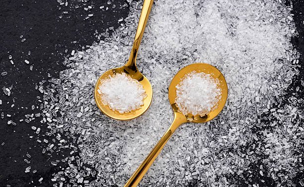 A container of Epsom Salt crystals with a scoop on a wooden surface.