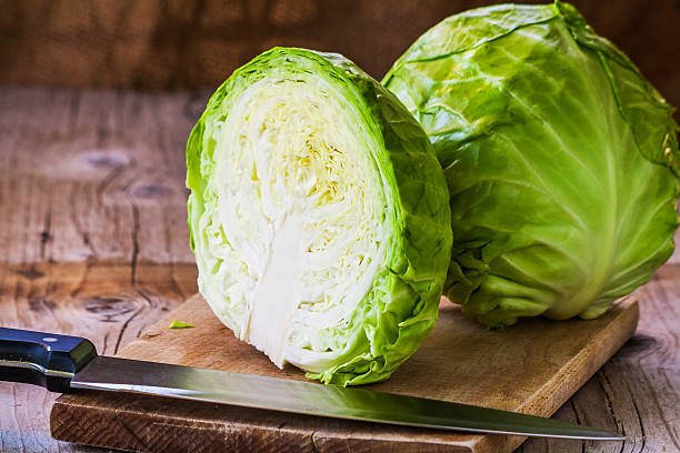 A fresh green cabbage cut in half showing its leafy interior on a white background.