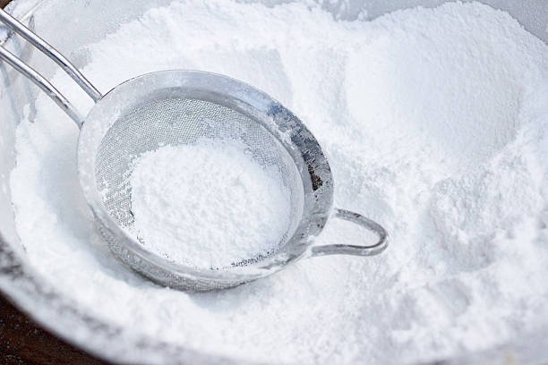 A bowl of fine white icing sugar with a spoon, ready for decorating desserts.