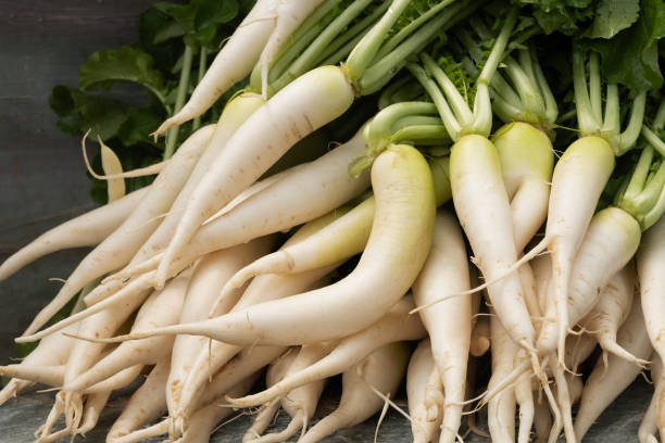 Fresh red radish slices with green leaves, showcasing their crunchy texture and vibrant color.