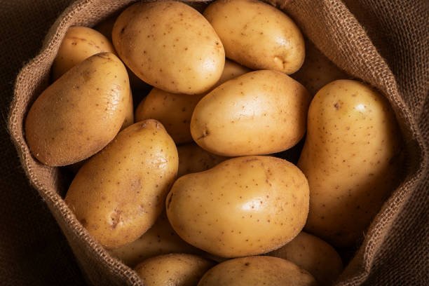 A basket of fresh, peeled potatoes on a rustic wooden surface.