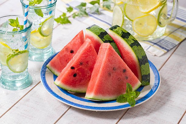 Juicy red watermelon slices with green rind arranged on a white plate.