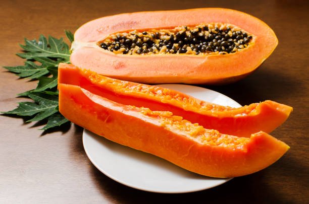 Ripe papaya fruit sliced open to reveal bright orange flesh and black seeds.