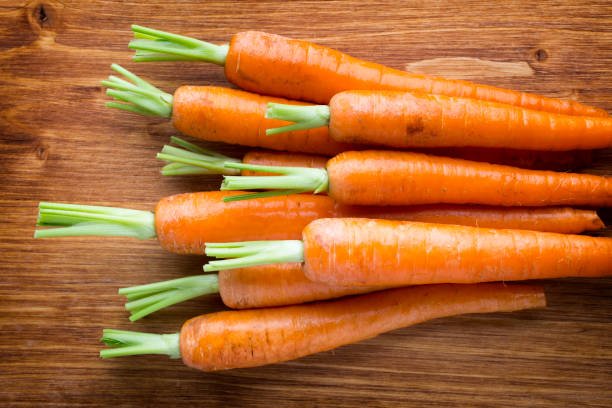 Fresh orange carrot with green leafy tops, showcasing its vibrant color and crisp texture.
